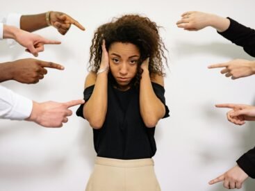 Stressed woman with hands on ears surrounded by pointing fingers, illustrating pressure.