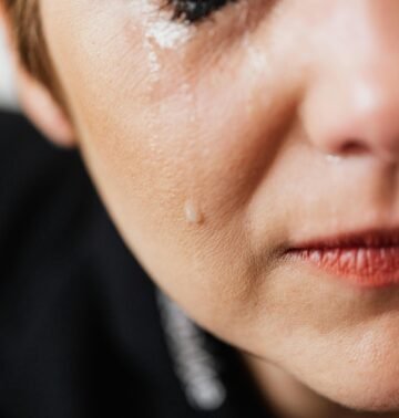 Closeup of crop anonymous sad adult female with makeup crying because of emotional problems