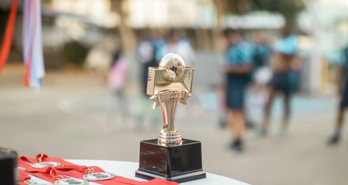 Close-up of a polished soccer trophy with medals at an outdoor sports award ceremony.