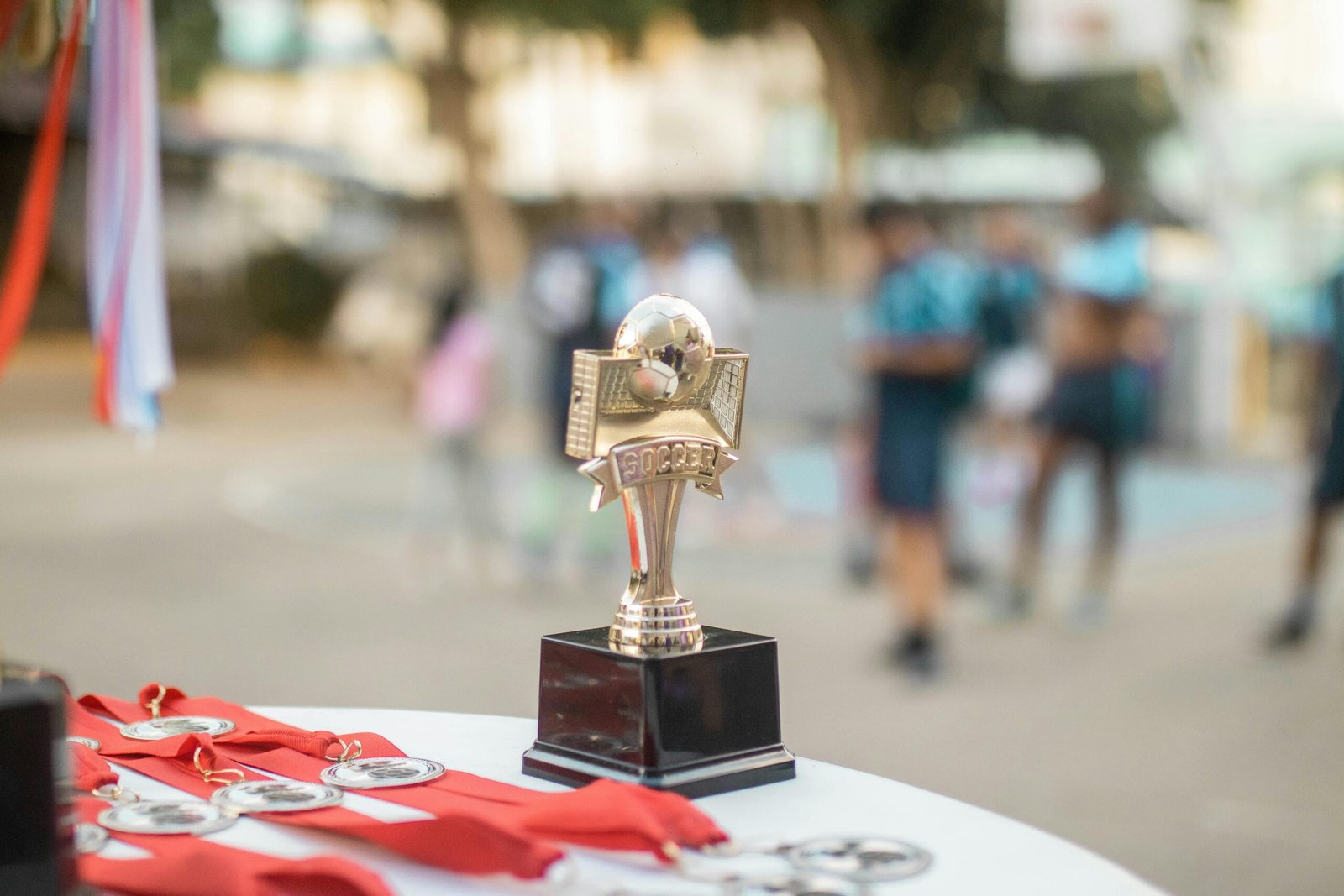 Close-up of a polished soccer trophy with medals at an outdoor sports award ceremony.