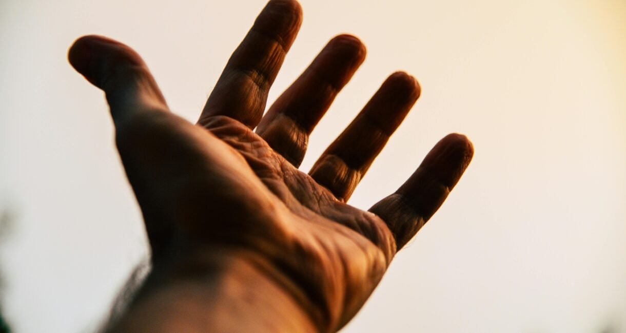 A human hand reaching toward the sky, silhouetted against a bright, warm backdrop.