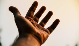 A human hand reaching toward the sky, silhouetted against a bright, warm backdrop.