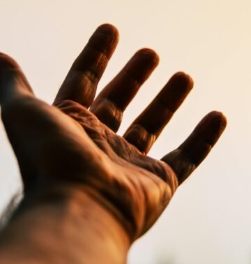 A human hand reaching toward the sky, silhouetted against a bright, warm backdrop.