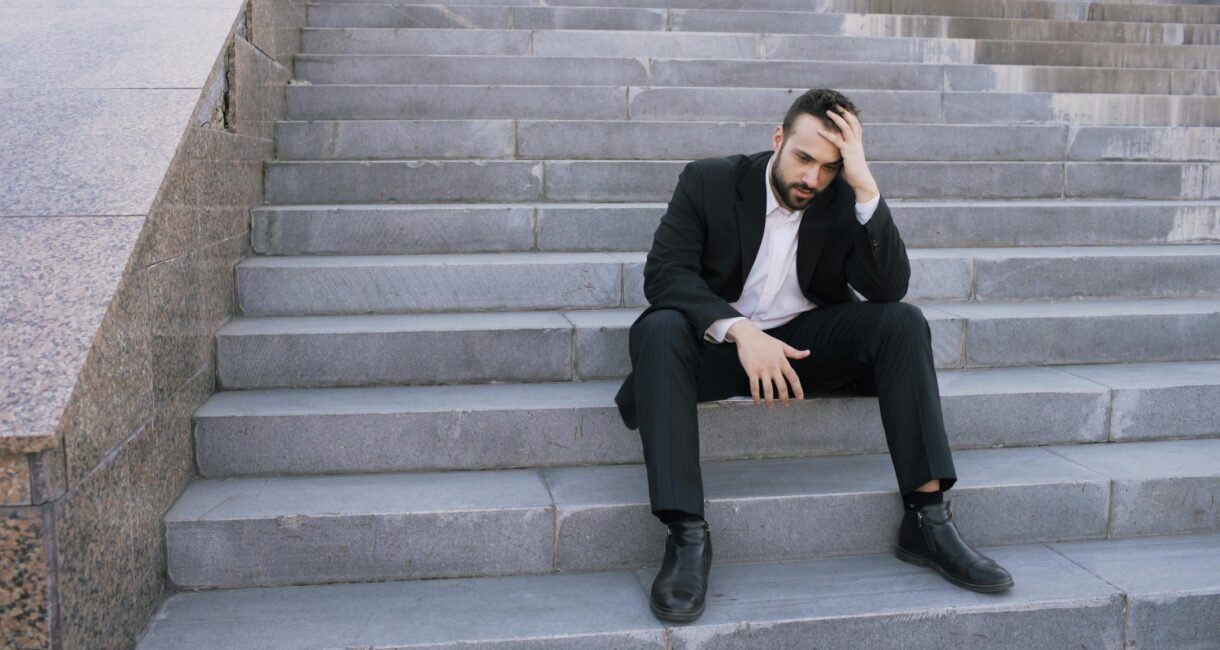 Businessman in a suit sitting distressed on concrete stairs, facing challenges.