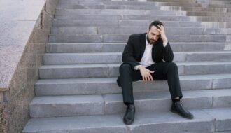 Businessman in a suit sitting distressed on concrete stairs, facing challenges.