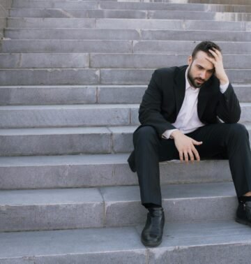 Businessman in a suit sitting distressed on concrete stairs, facing challenges.