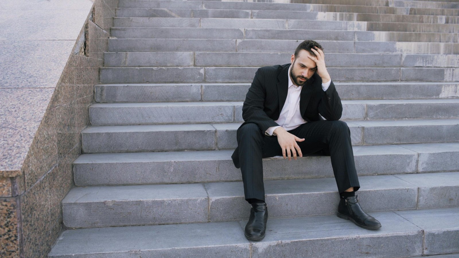 Businessman in a suit sitting distressed on concrete stairs, facing challenges.