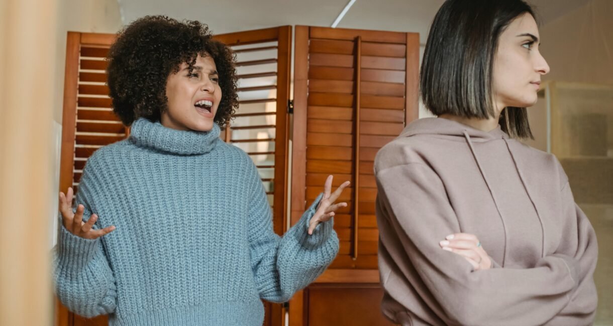 Furious African American female with black hair screaming while fighting with displeased female in light room with wooden folding screen