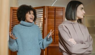 Furious African American female with black hair screaming while fighting with displeased female in light room with wooden folding screen