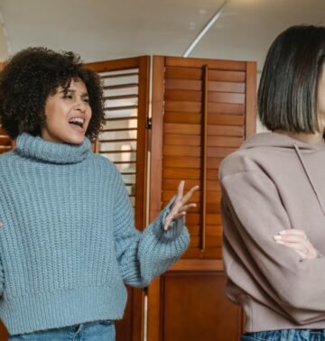 Furious African American female with black hair screaming while fighting with displeased female in light room with wooden folding screen