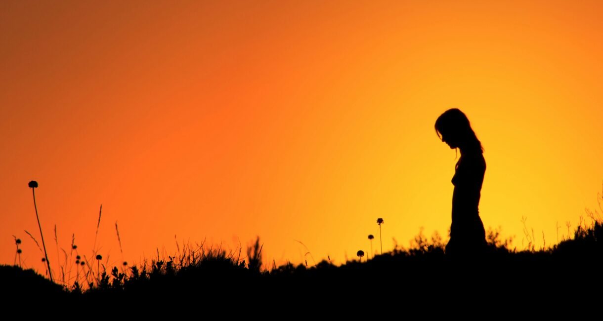 Silhouette of a woman standing in a field during a vibrant orange sunset.