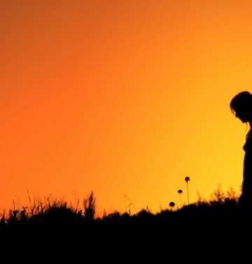 Silhouette of a woman standing in a field during a vibrant orange sunset.