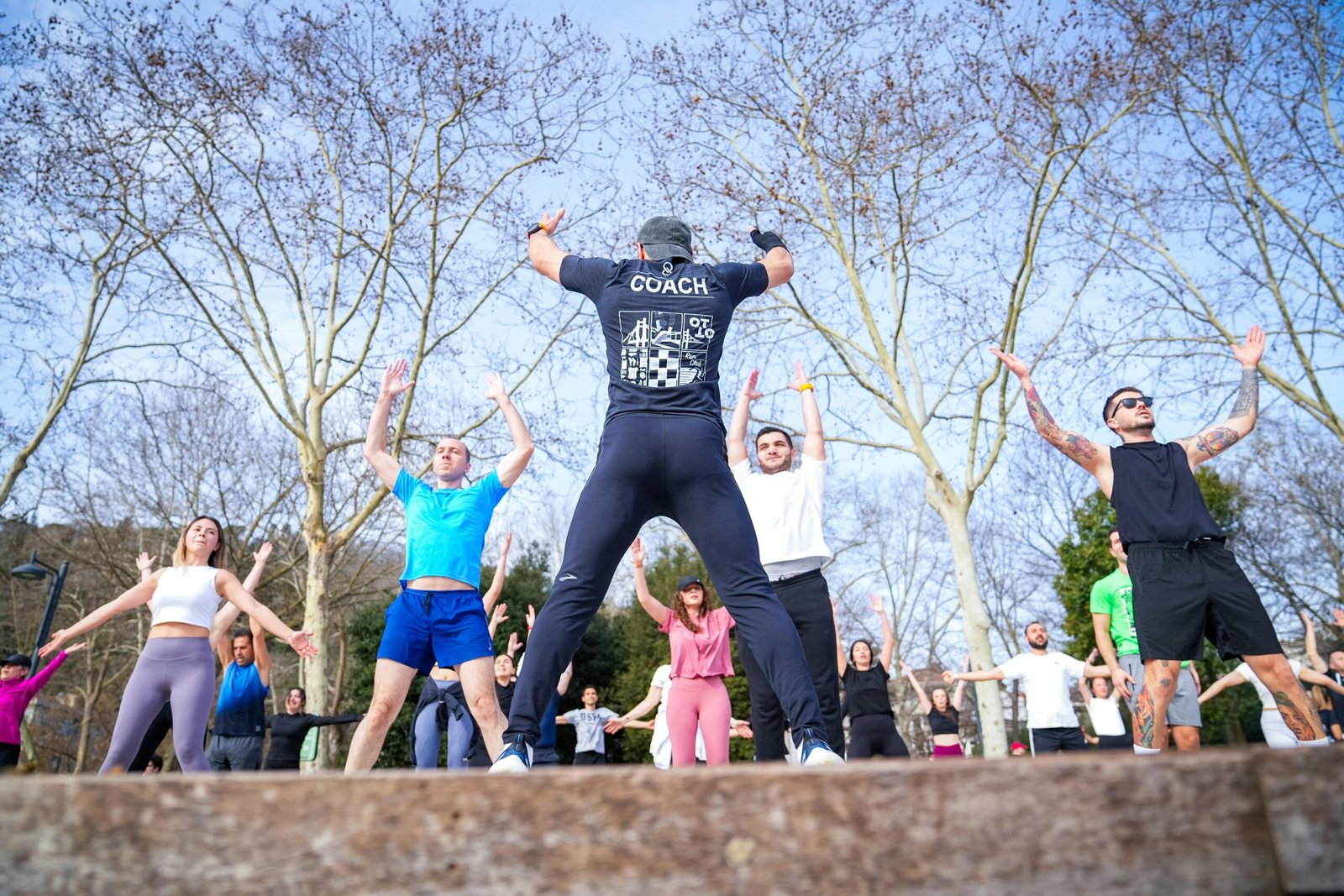 Group exercise session in a sunny Istanbul park led by a fitness coach outdoors.