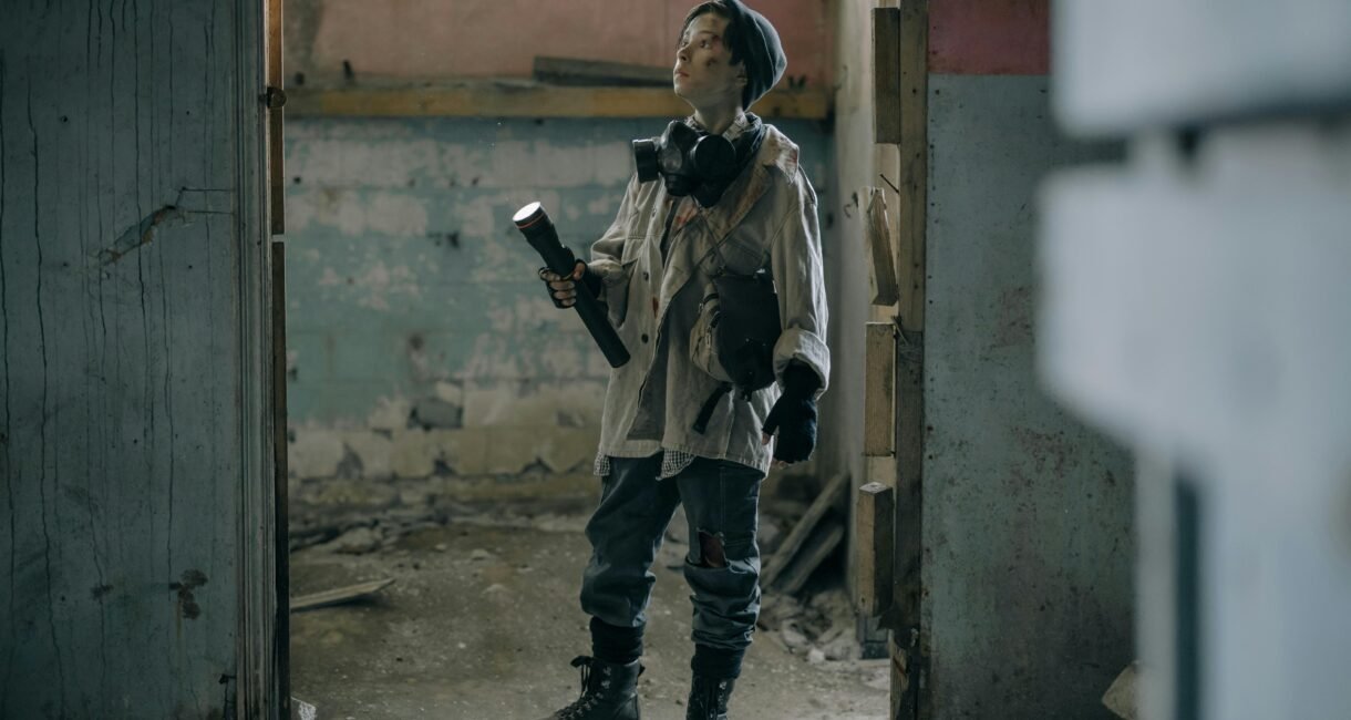 Young explorer in a gas mask investigates a ruined, desolate building with a flashlight.