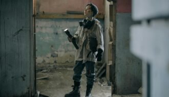 Young explorer in a gas mask investigates a ruined, desolate building with a flashlight.