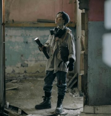 Young explorer in a gas mask investigates a ruined, desolate building with a flashlight.