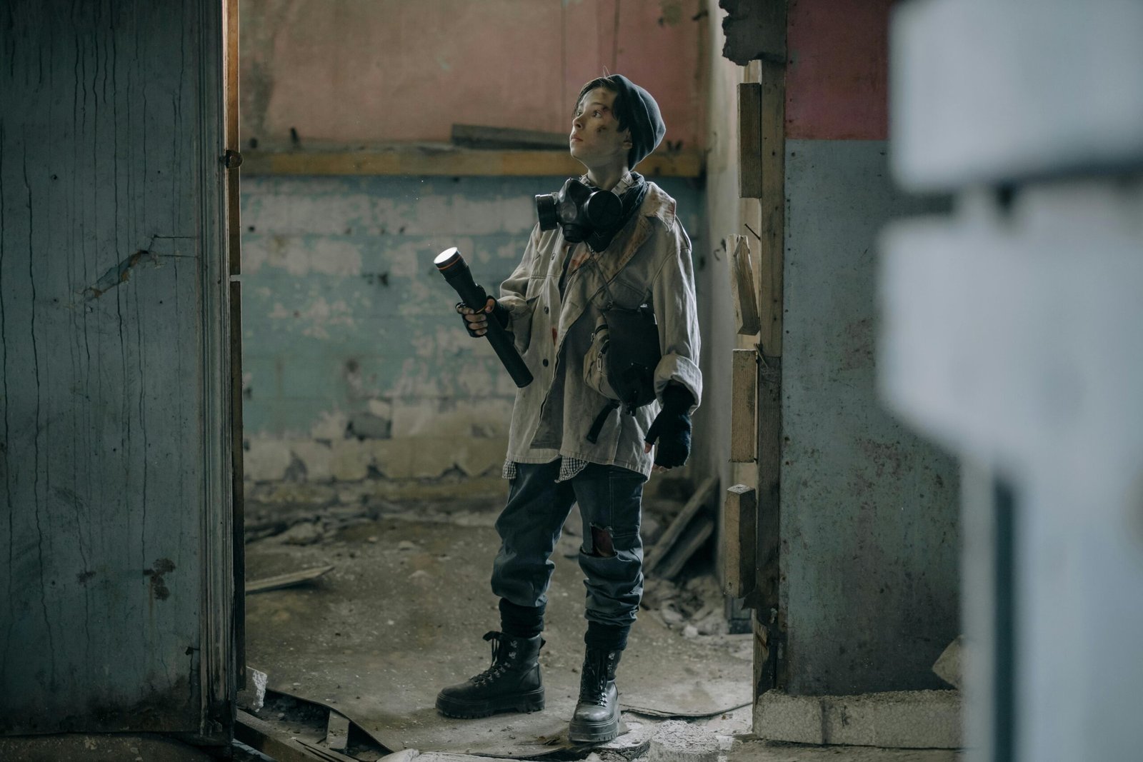 Young explorer in a gas mask investigates a ruined, desolate building with a flashlight.