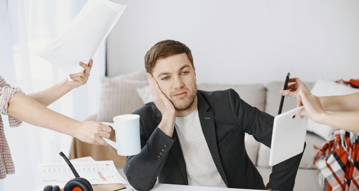 A businessman overwhelmed by tasks in a modern office setting, depicting multitasking and stress.