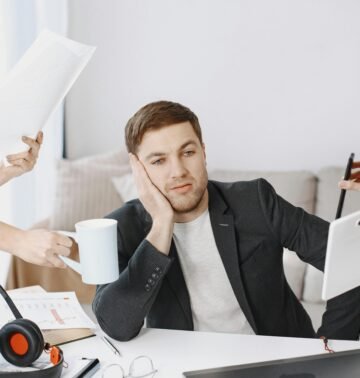 A businessman overwhelmed by tasks in a modern office setting, depicting multitasking and stress.